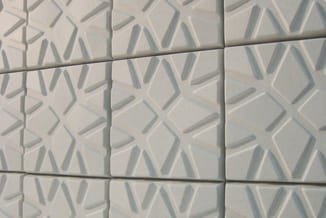 Witte keramische wandtegels met gestructureerd driehoeken- en diamantpatroon, in raster geplaatst.