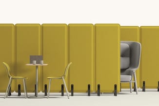 Gele akoestische panelen met daarvoor twee gele stoelen aan een klein tafeltje en een grijze fauteuilwagen met hoge rugleunin