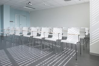 Moderne vergaderruimte met witte stapelstoelen met grijze metalen frame, op tegelvloer bij raam met zonwering.