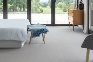 Moderne slaapkamer met grijs-witte bank, houten nachtkastje, blauwe gebreide plaid, houten stoelen en groot raam met uitzicht