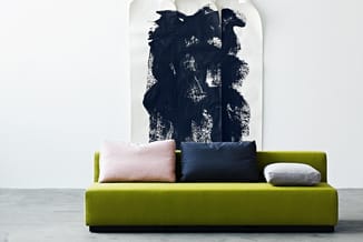 Groene sofa met drie kussens (roze, donkerblauw, grijs) tegen witte muur met donkerblauw abstract kunstwerk.
