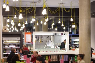 Modern café-interieur met gele hangende verlichting, witte werkplek met gereedschap, betonnen kolom, bezoekers aan tafels, pr