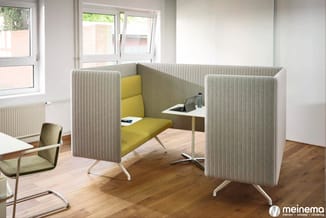 Akoestische belcel met grijsgroen stofbekleding en gele zitbank, wit werkblad, in kantoorruimte met houten vloer.
