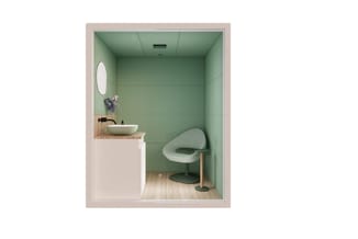Kleine werkruimte met groene wanden, witte wastafel op houten blad, ronde spiegel, grijze moderne stoel en houten vloer.
