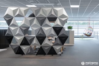 Modulair akoestisch scherm in driehoekige elementen, wit, grijs en zwart, in modern kantoor met bureaus en hangstoel bij raam