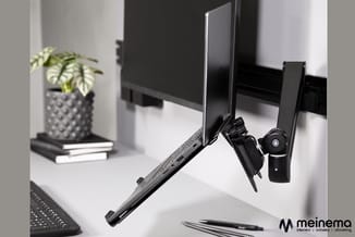 Monitor-arm met zwarte webcam op wit bureau, kantoorplant en toetsenbord zichtbaar in minimalistisch werkplekontwerp.