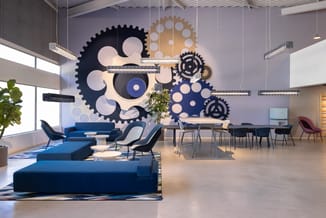 Modern kantoorinterieur met blauwe hoekbank, grijze stoelen, vergadertafel en grote muursculptuur met zwarte en gouden tandwi