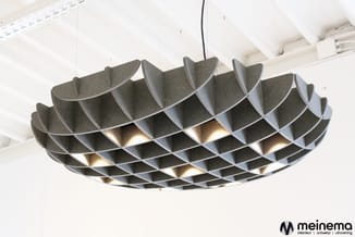 Grijze akoestische hanglamp met geometrische vlechtstructuur en ingebouwde verlichting tegen wit plafond met balken.