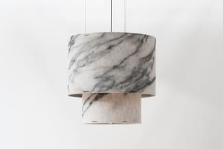 Hangende cilindervormige pendant lamp met marmeren print in grijs en wit, dubbele scherm constructie tegen witte wand.
