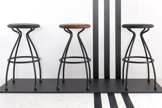 Drie designbarkrukken met zwart metalen frame en voetsteun. Linker en rechter kruk hebben zwart zitoppervlak, middelste kruk