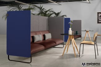 Kantoorlounge met bordeauxrood leren bank, blauwe en grijze akoestische schermen, houten tafels en houten stoel.