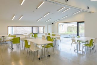 Moderne vergaderruimte met verrijdbare tafels, groene stoelen, lijnverlichting, grote ramen en grijze vloer.