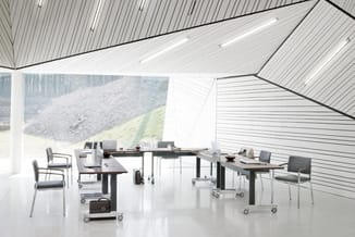 Modern kantoor met zwarte vergadertafels, grijze stoelen op wielen, witte vloer en akoestisch plafond met lijnenpatroon.