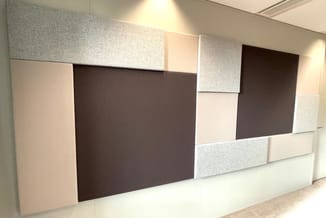 Wandpanelen in grijs, beige en donkerbruin met verschillende oppervlaktetexturen, modulair op kantoorwand gemonteerd.