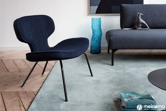Donkerblauwe design fauteuil met vleugelvormige rugleuning en metalen poten in moderne woonruimte met grijze bank en houten v