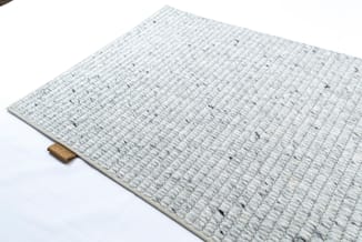 Lichtgrijze rechthoekige vloermat met geribde textuur en goudkleurig label aan zijkant, tegen witte achtergrond.
