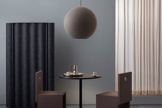 Minimalistisch ingerichte ruimte met twee bruine stoelen aan rond zwart tafeltje, grijze hanglamp, donkerblauwe gordijnen lin