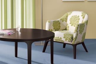 Ronde zwarte tafel met groene fauteuil met bloemenpatroon in kantoorruimte met beige wand en groene gordijnen.