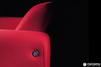 Rode stofbeklede fauteuil met ergonomische rugleuning en bedieningsknop, gefotografeerd tegen zwarte achtergrond.