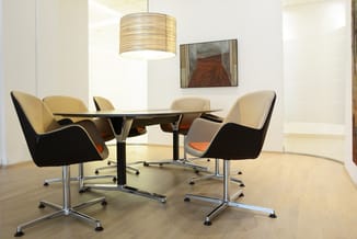 Moderne vergaderkamer met zwart glazen tafel, vier design stoelen in beige en zwart met oranje accenten, hangende ronde lamp,