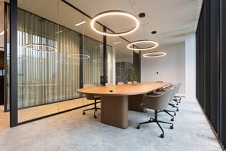 Moderne vergaderruimte met houten ovale vergadertafel, grijze bureaukstoelen met wieltjes, glazen wanden, ronde hangende LED-