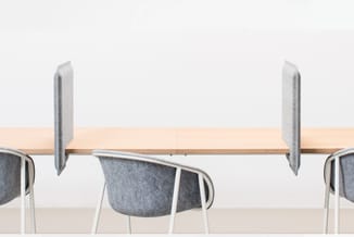 Houten vergadertafel met grijze akoestische schermen en stoelen met grijze bekleding in kantooromgeving.