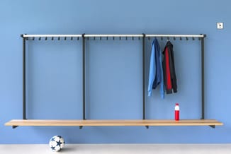 Wandmontagesysteem met drie verticale buizen, houten plank, haakjes en kledinghangers met jacks. Rode fles en voetbal onderaa