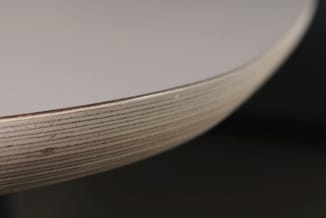 Detailshot houten tafelrand met houtnerf en metalen afwerkingsprofiel op donkere achtergrond.