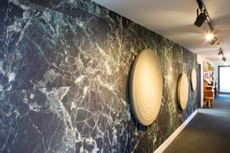 Corridor met donker marmeren wand en twee ronde wandlampen met warmwit licht, track lighting aan plafond.