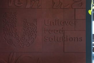 Terracotta gekleurde wandpanelen met ingraveerde tekst "Unilever Food Solutions" en decoratieve fruit- en plantenafbeeldingen
