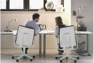 Twee personen aan een bureau met witte ergonomische bureaustoel met rode accenten, grijze bureau, lamp en computer. Moderne k