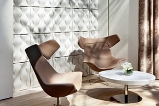 Modern lounge-hoek met twee bruine fauteuils en wit rond bijzettafeltje tegen witte 3D-wandpanelen.