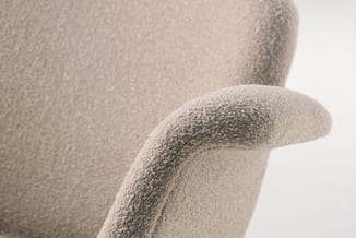 Grijsbeige gestoffeerde fauteuil met gestructureerde stofbekleding en afgeronde armleuning, detail close-up.