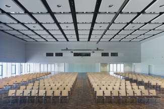 Lege presentatieruimte met rijen beige stoelen op houten vloer, moderne plafondstructuur met zwarte balken en inbouwverlichti