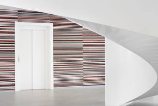 Moderne kantoorruimte met witte deur, gestreepte wand in rood-zwart-wit patroon en golvend wit plafond.