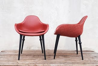 Twee rode stoelen met zwarte poten tegen witte muur op houten vloer. Vooraanzicht en zijaanzicht.