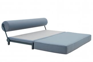 Grijsblauw bed met cilindervormige hoofdsteun, zwart metalen frame en lichte matras tegen witte achtergrond.