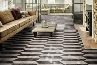 Moderne woonkamer met caramelkleurige leren bank links, grijsgroene hoekbank rechts, geometrisch zwart-wit patroon tegelvloer