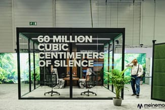 Moderne belcel met glazen wanden, zwart frame, twee bureaustoelen, plantenbak, groene wandbekleding en tekst "60 MILLION CUBI