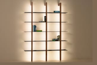 Modulair kastensysteem met drie houten verticale delen en zes zwarte horizontale legplanken, gevuld met boeken. Indirecte ach
