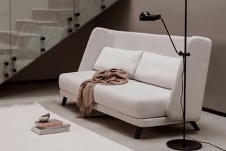 Witte modulaire bank met beige plaid in minimalistische ruimte, zwarte boogvloerlamp en stapel boeken op vloer.