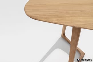 Ronde houten tafel met natuurlijke eiken afwerking en minimalistisch onderstel, gedeeltelijk zichtbaar tegen witte achtergron