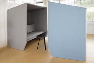 Grijze en blauwe akoestische boxen in kantoor; grijze box bevat zithoek met bank en zwarte stoel, houten vloer.