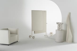 Minimalistische kantoorinrichting met beige/crème stoffen fauteuil, mobiel scherm, cilindervormige poef, decoratieve manden e