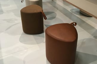 Bruine poefjes met leren zitting en textielkant, met handvaten, op licht marmoleum vloer in kantoor.