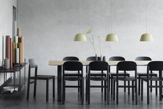Moderne vergaderruimte met lange houttafel, zwarte stoelen, drie hangende gele koepellampen en betonnen wand met kleurige mat
