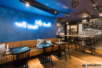 Modern kantoor met blauwe wand, cognackleurige boxen, zwarte stoelen, houten vloer en neonreclame.