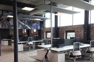 Modern kantoor met witte bureaus, zwarte ergonomische stoelen, bakstenen muur, grote ramen, verlichte plafondpanelen en zwart