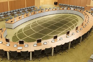 Moderne vergaderruimte met grote houten vergadertafel in ovale vorm, zwarte bureaustolen, houten wandbekleding, groene vloerb