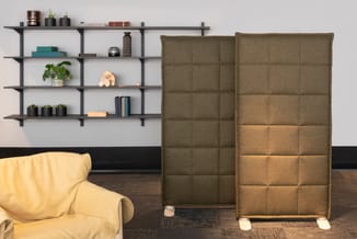 Twee bruine geluidsschermen met quilted stoffering in kantooromgeving, naast gele fauteuil en wandplanken met decoratie.